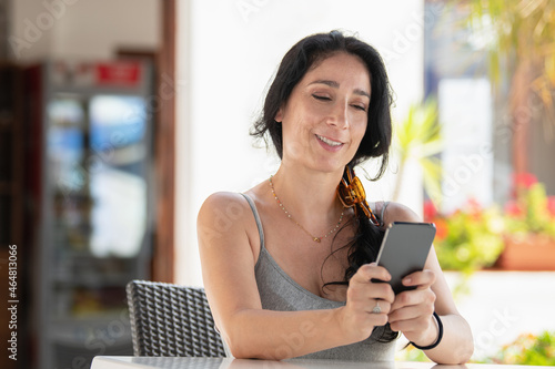 Adult woman smiling sitting in a cafe outside using phone with both hand