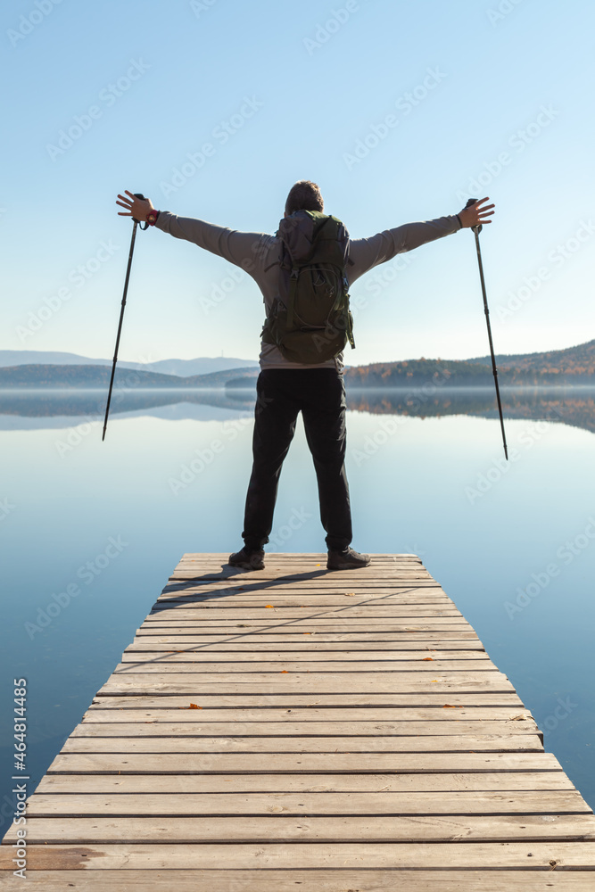 A man admires the landscape of a mountain lake while standing on the pier