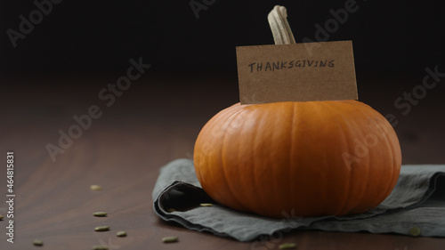 Slow motion man hand put thanksgving card next to orange pumpkin on walnut table photo