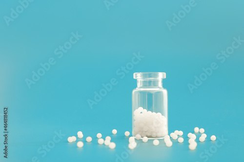 Close-up image of homeopathic globules in glass bottle on blue background. Homeopathy pharmacy, herbal, natural medicine, alternative homeopathy medicine, healthcare. Free space, copy space. photo