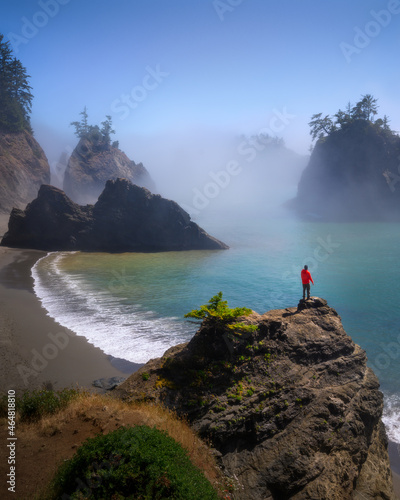 Man looking out beautiful sea stacked rocks and fog in summer at Secret Beach, Oregon photo