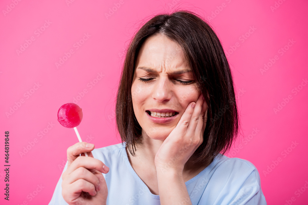 Young woman with sensitive teeth eating sweet lollipop on color background Young woman with sensitive teeth eating sweet lollipop on color background