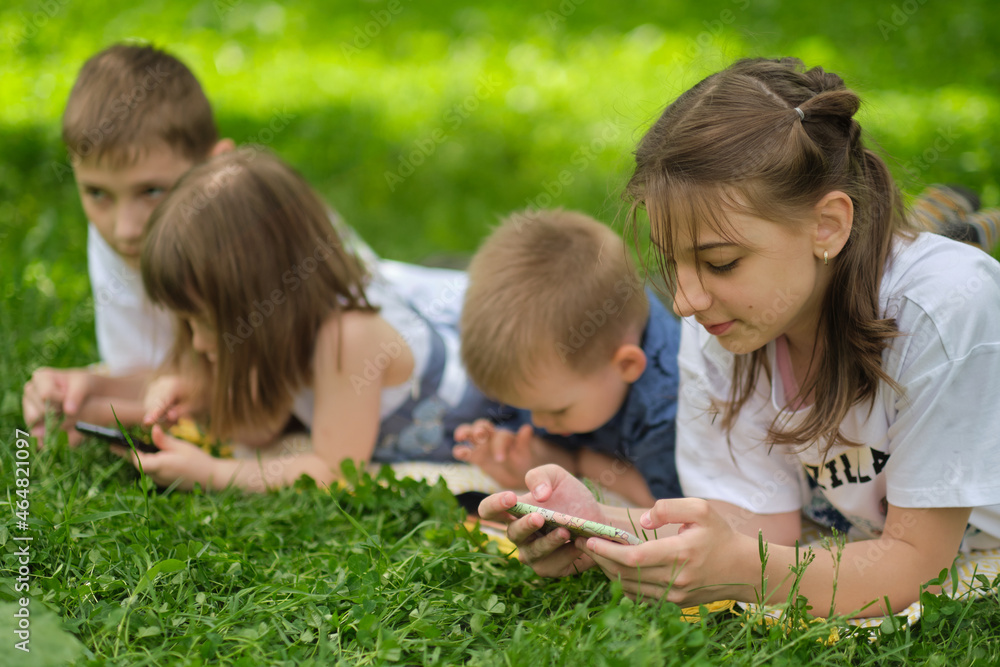 children friend group playing internet with mobile smartphone on grass. Happy children using smartphones sitting on the grass. Brothers and sister. children friend group playing internet with mobile smartphone on grass. Happy children using smartphones sitting on the grass. Brothers and sister.