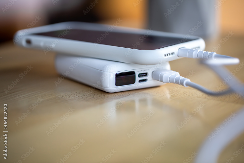 A smartphone is charged from a small white power bank. A smartphone is charged from a small white power bank.