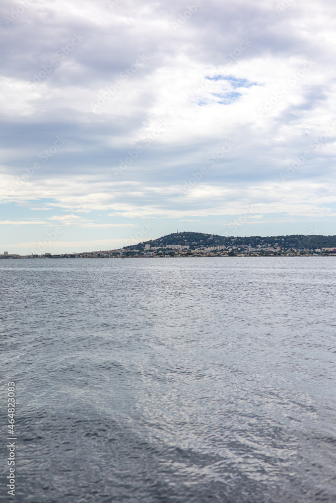 Obraz premium Vue par temps nuageux sur Sète et le Mont Saint-Clair, sur bord de l’Étang de Thau, depuis les parcs à huîtres (Occitanie, France)