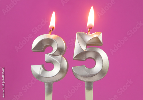 Burning silver birthday candles on pink background, number 35