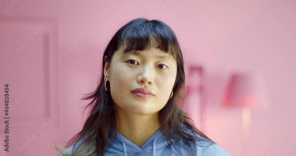 Portrait of a beautiful young Asian woman standing in a pink monochrome studio looking at camera. Headshot of positive female model standing confident at home with rose color interior design Portrait of a beautiful young Asian woman standing in a pink monochrome studio looking at camera. Headshot of positive female model standing confident at home with rose color interior design