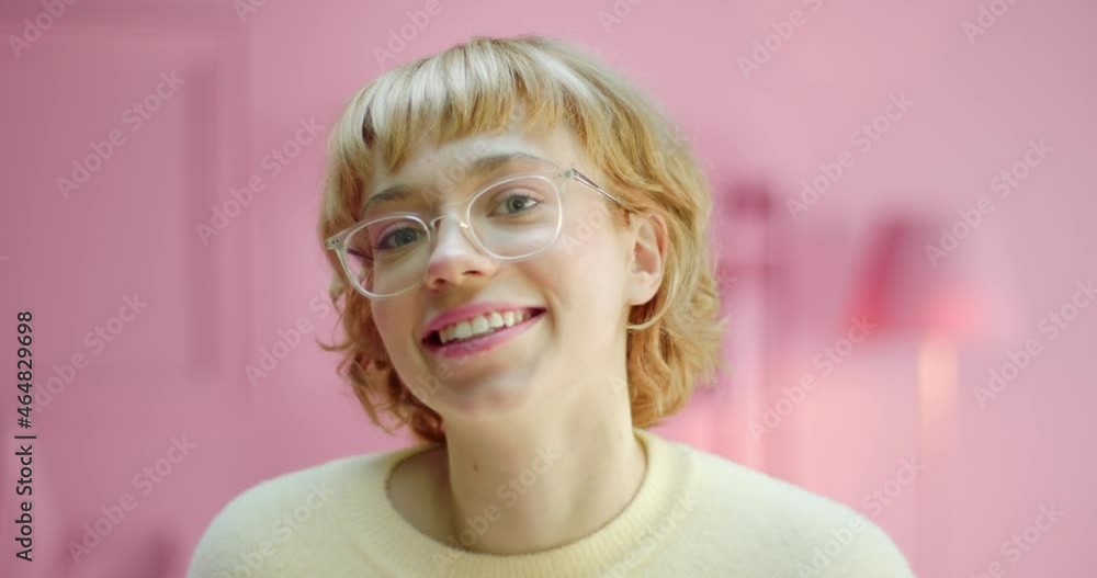Happy young Caucasian female model showing smile looking at the camera in pink monochrome studio interior. Attractive cheerful pretty blonde hair woman standing at rose color home decoration Happy young Caucasian female model showing smile looking at the camera in pink monochrome studio interior. Attractive cheerful pretty blonde hair woman standing at rose color home decoration