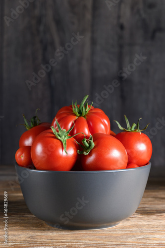 Ripe raw red tomatoes in a bowl on rustic wooden table. Side view
