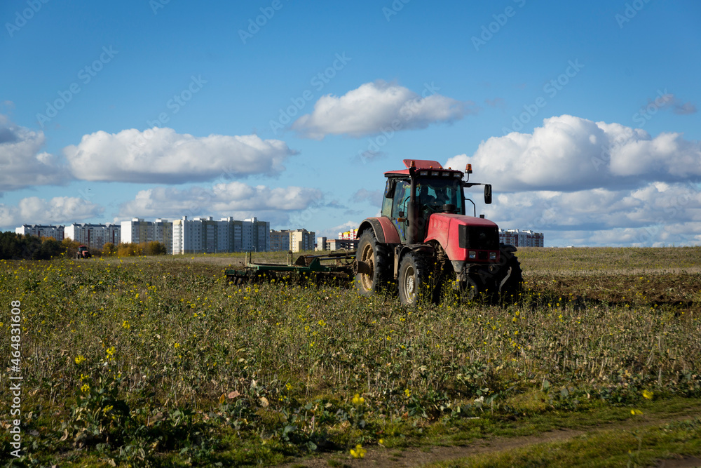 Fototapeta premium A farmer in a tractor, agricultural machinery, prepares the land with a cultivator. A modern red tractor in a field. Plowing a heavy tractor while cultivating agricultural work in a field with a plow.