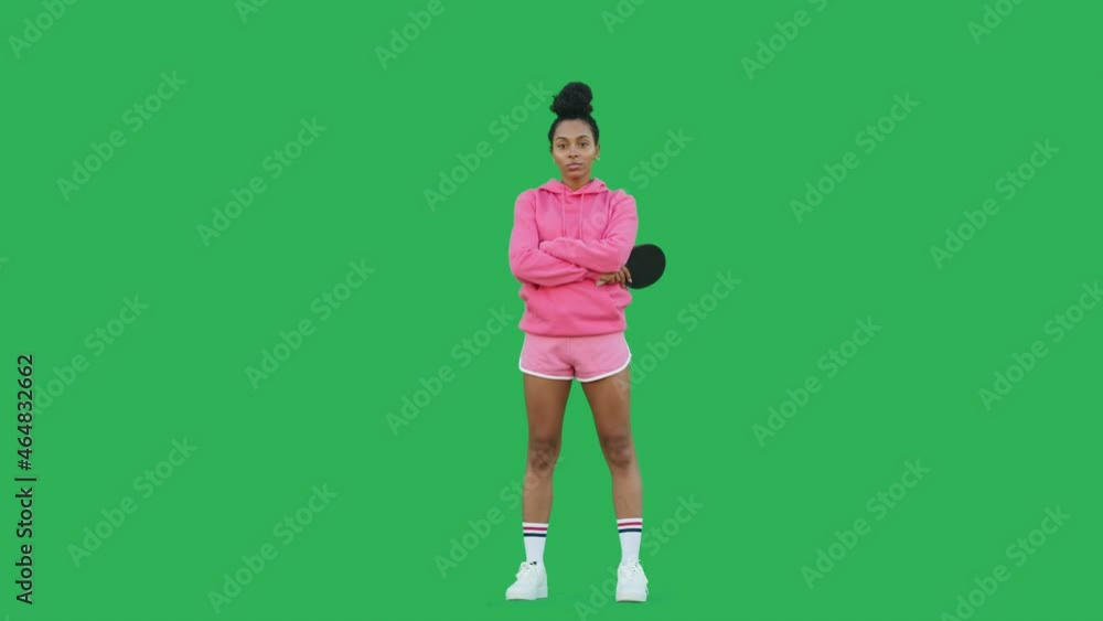 Young woman table tennis player with racket over green background. Portrait of african american girl wearing pink hoodie and shorts looking at camera. Chroma key. Young woman table tennis player with racket over green background. Portrait of african american girl wearing pink hoodie and shorts looking at camera. Chroma key.