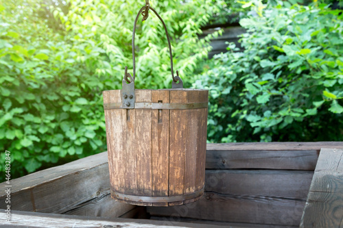 Wooden well with a bucket on a chain on background of green trees. © ALEXEY