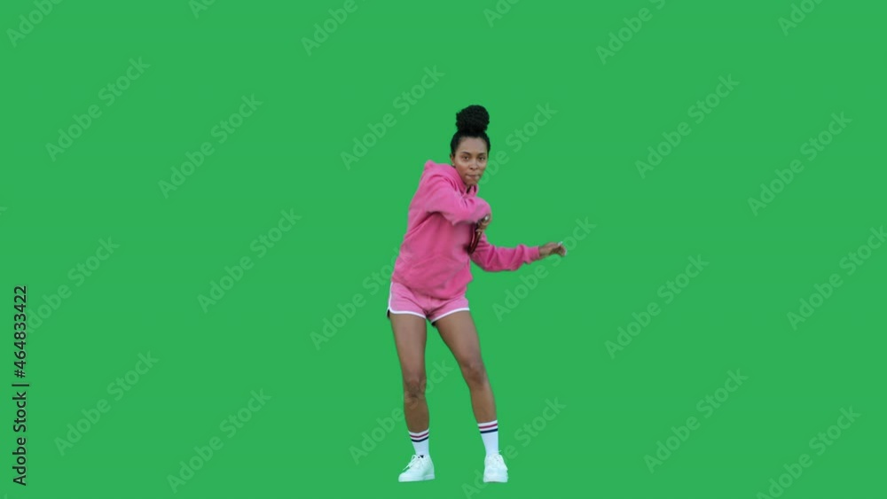 Young woman table tennis player training or playing over green background. African american girl wearing pink hoodie and shorts having fun with racket. Chroma key. 4k raw video footage