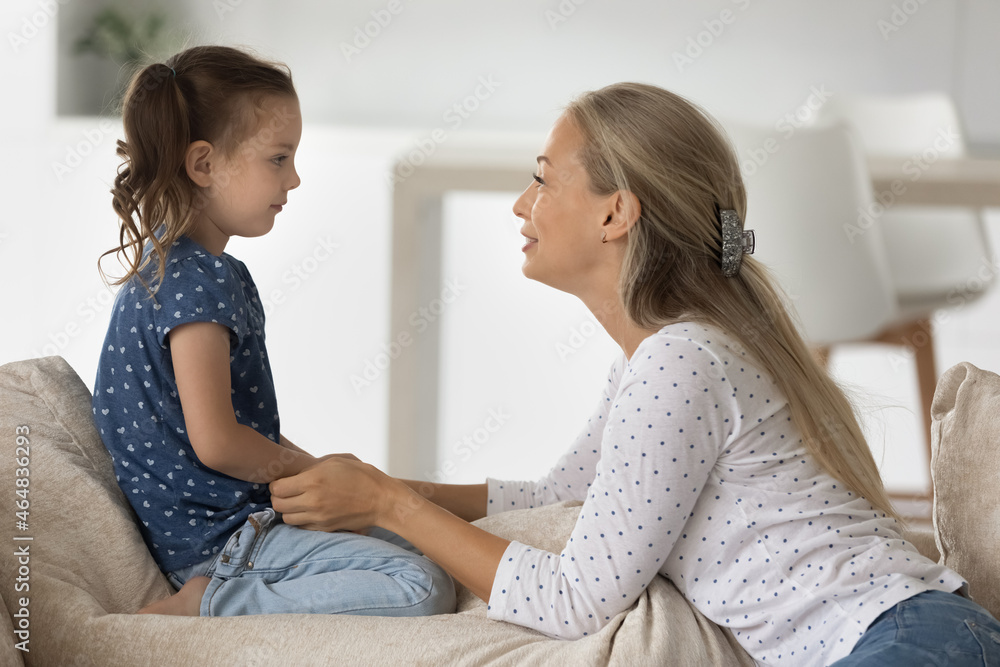 Side view smiling young woman holding hands of little cute kid daughter, involved in sincere conversation at home, helping solving problems or giving advices, trustful family relations concept. Side view smiling young woman holding hands of little cute kid daughter, involved in sincere conversation at home, helping solving problems or giving advices, trustful family relations concept.