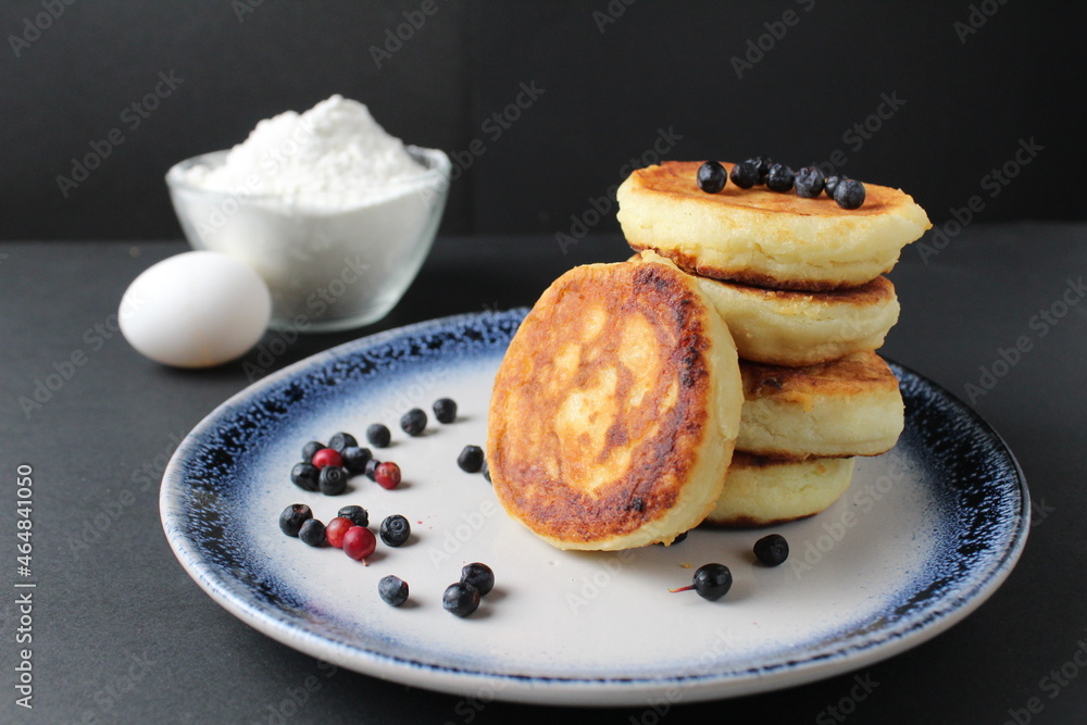 breakfast pancakes cheesecakes are stacked slide on a plate with blueberries blueberries cherries. Traditional breakfast Russian Slavic in the background is egg flour. Cooking breakfast breakfast pancakes cheesecakes are stacked slide on a plate with blueberries blueberries cherries. Traditional breakfast Russian Slavic in the background is egg flour. Cooking breakfast