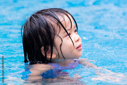 Headshot of little girl in blue pool. Relaxing time. Summer season. Happy child playing swimming water park. Kid aged 4-5 years old.