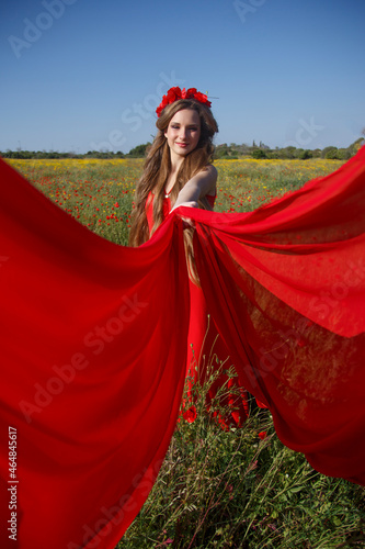 Young beautiful woman walking through a poppy field at sunset