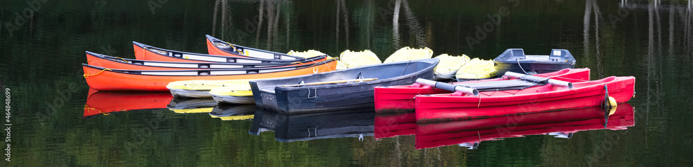 Red blue and yellow kayak canoes in row moored at lake
