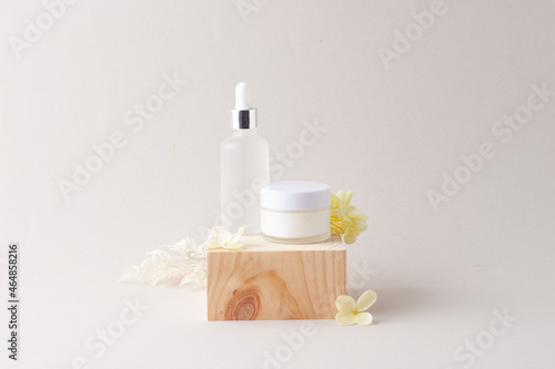 Cosmetic skin care products with wood podium and flowers on grey background. Close up  copy space