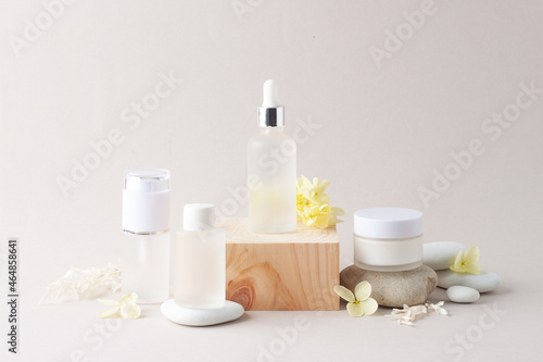 Cosmetic skin care products with wood podium and flowers, stone on grey background. Close up, copy space