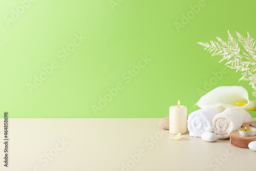 Spa treatment with candles, towel and flowers on green background. Close up, copy space