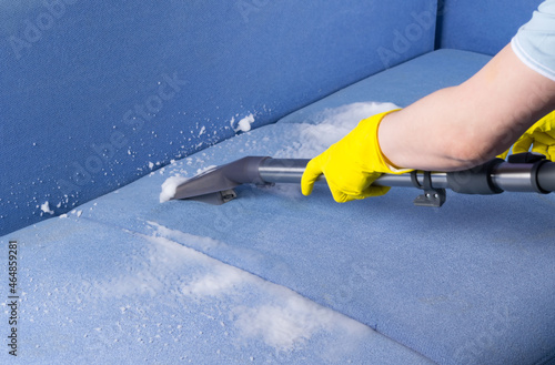 specialist in protective gloves, cleans the dirty surface of the sofa fabric with a washing vacuum cleaner and foam photo