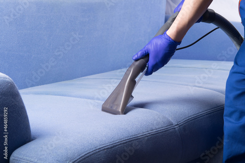 specialist in protective gloves, cleans the fabric of the sofa with a washing vacuum cleaner and foam photo