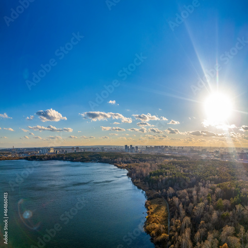 Autumn forest on lake shore at sunset and city on horizon, auerial view
