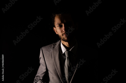 A young businessman in a smart gray suit looking at the camera with moody lighting that casts half of him into shadow