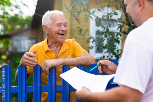 Grandfather talking to census agent standing at fence of his country house photo