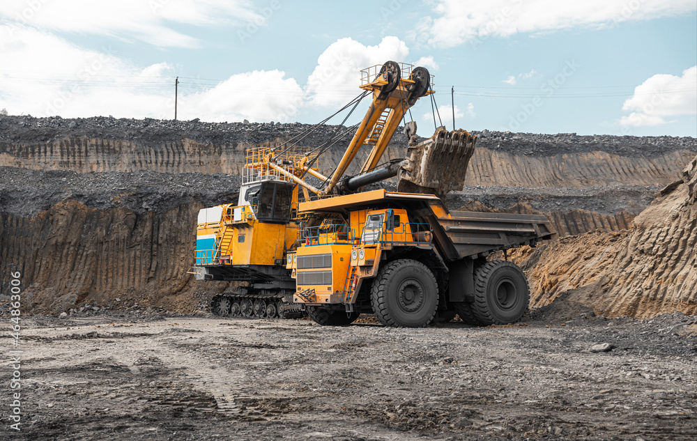 Fototapeta premium Large quarry dump truck. Big yellow mining truck at work site. Loading coal into body truck. Production useful minerals. Mining truck mining machinery to transport coal from open-pit production