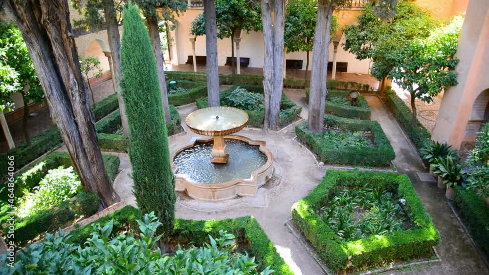 Aerial view of a green patio with trees and gardens in the famous Alhambra, Granada, Spain. In the middle an ancient fountain with water flowing is visible. Aerial view of a green patio with trees and gardens in the famous Alhambra, Granada, Spain. In the middle an ancient fountain with water flowing is visible.