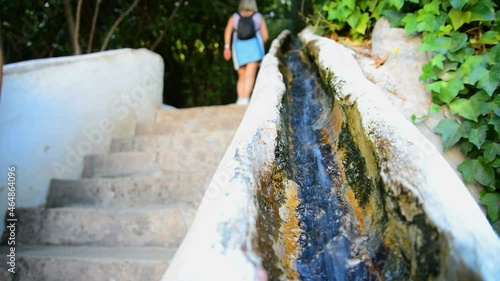 The water is flowing in a parapet of a staircase in the famous Alhambra mansion, Granada, Spain. On the blurred background people and tourists are walking. Selective focus.