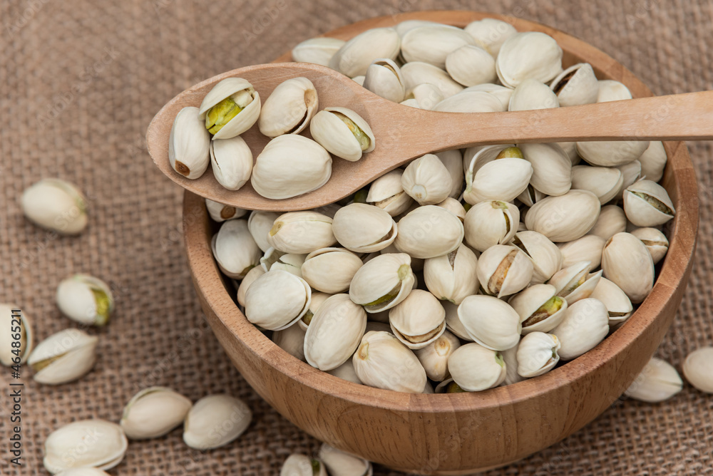 Pistachios in wooden spoon and wooden bowl.