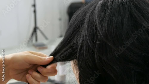 Woman hairdresser combing long black curls with a comb. Hairdresser combing hair strand while hairstyling in beauty salon. Make hairdo for long haired woman. Beauty concept