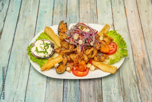 Peruvian seafood jelly tray with cassava, battered mussels, cooked and fried prawns, scallops in sauce, and fresh vegetables photo