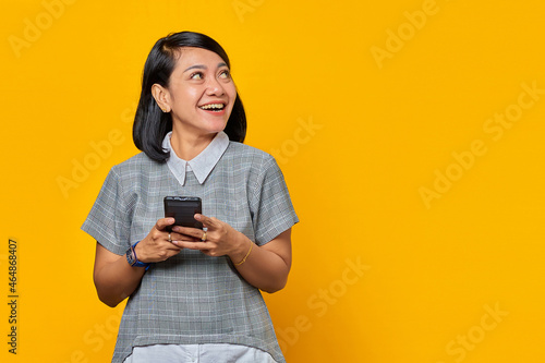 Portrait of smiling young Asian woman holding cell phone and looking aside