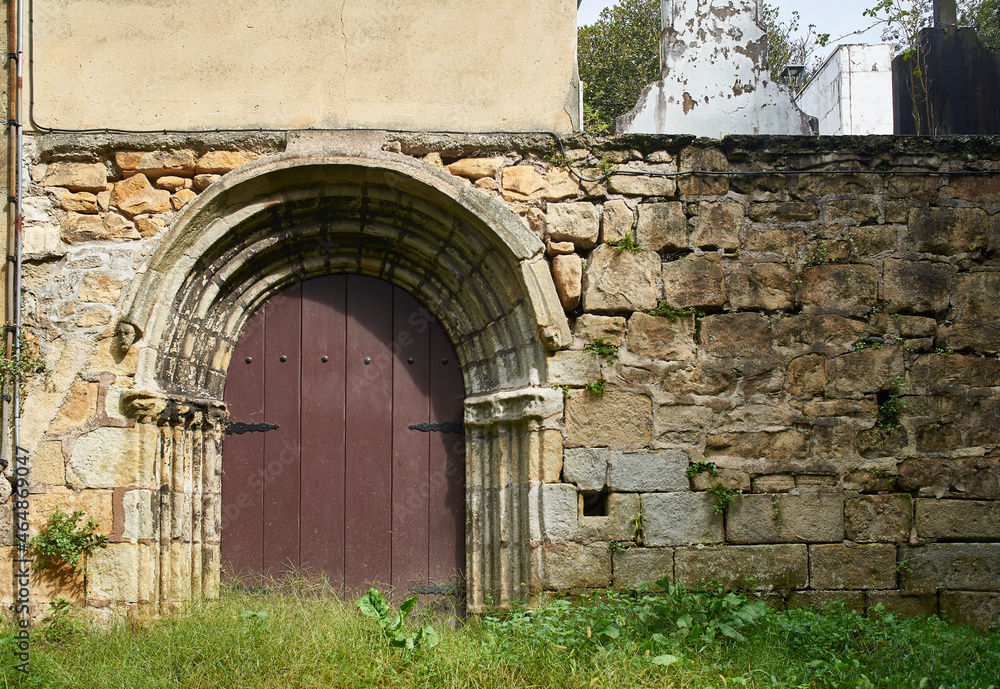 Fototapeta premium Antique Romanesque door on a rustic stone wall of a historic building in a European village, with five decorated with archivolts and baquettes finished with theriomorphic faces.