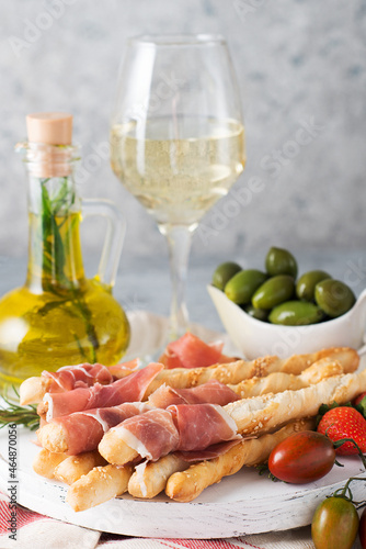 Traditional Italian snacks for wine, breadsticks (grissini), tomatoes, prosciutto (jamon), strawberries and olives. Selective focus.