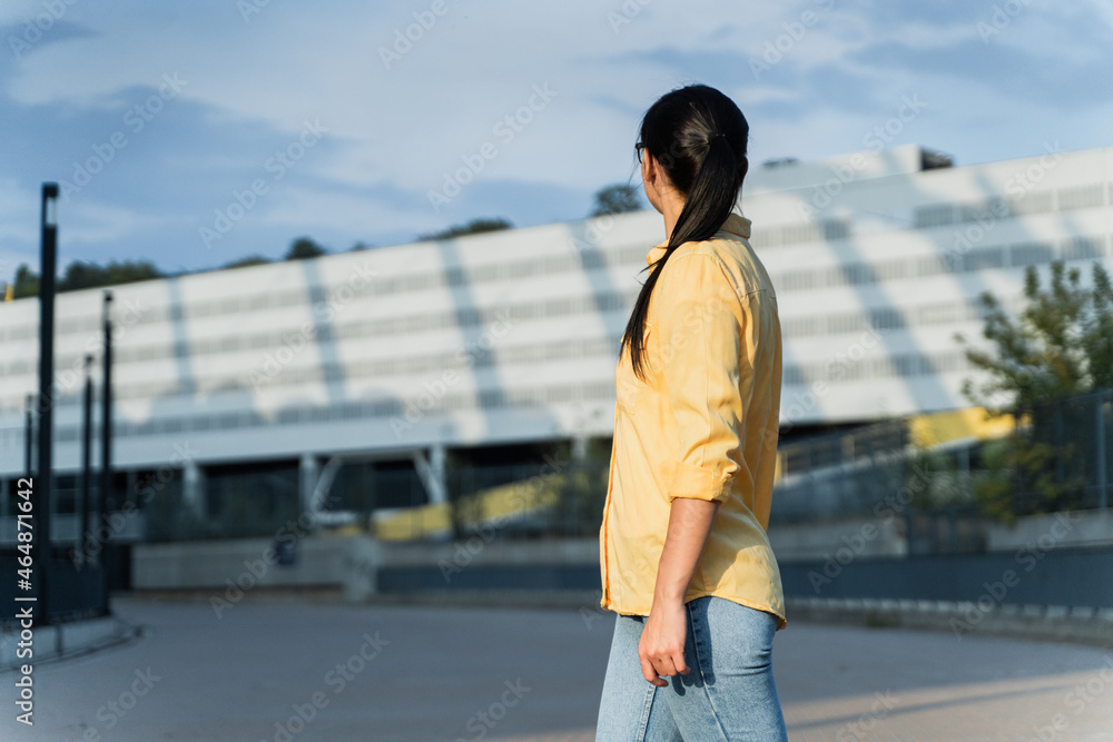 Back view of the lonely and pensive woman looking away while walking at the street during the summer day. Outdoor shot. Stock photo