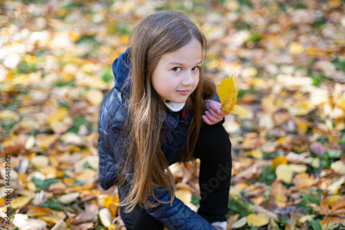 Girl collects leaves in autumn park. Portrait of cute little blond child outdoors. Beautiful smiling kid having fun on a warm fall day. Happy childhood.