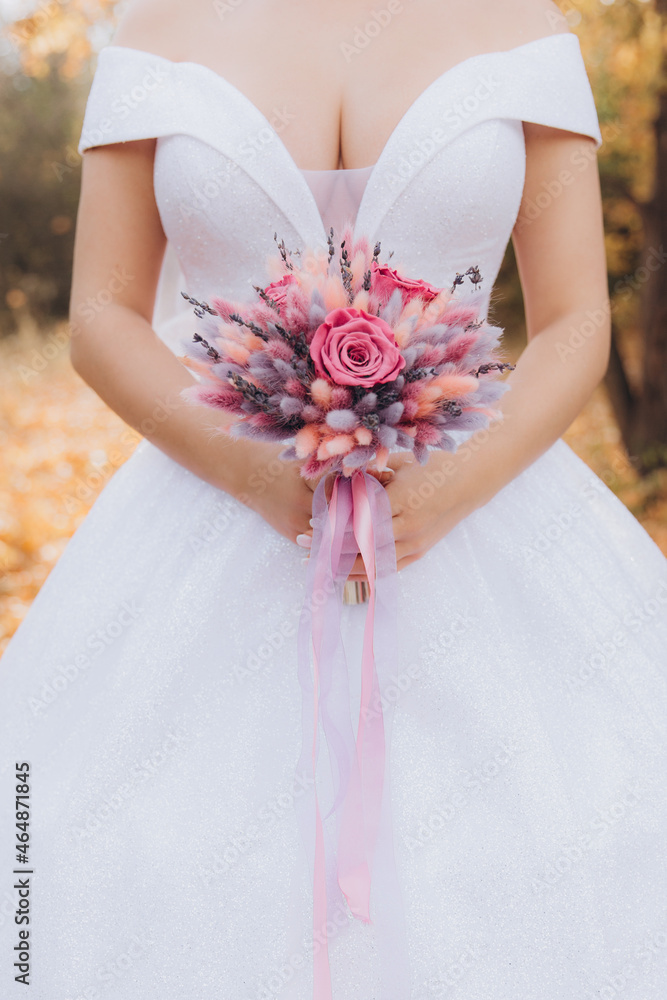 Autumn pink wedding bouquet with pink ribbons in the hands of the bride in a white wedding dress. Autumn pink wedding bouquet with pink ribbons in the hands of the bride in a white wedding dress.