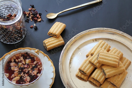 porcelain cup with fruit tea, loose fruit tea, white cup with golden decorations, chocolate-stuffed shortbreads, glass container with fruit tea