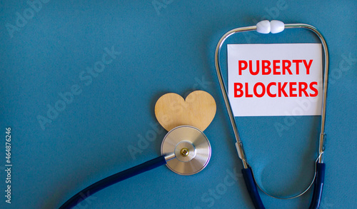 Medical and puberty blockers symbol. White card with words 'puberty blockers'. Wooden heart and stethoscope. Beautiful white background. Copy space. Medical and puberty blockers concept. photo