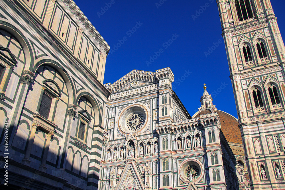 The elaborated facade of the Cathedral of Santa Maria del Fiore in Florence, Firenze, Italy, with the Bell Tower and detail of the Dome and deep blue sky in background.
