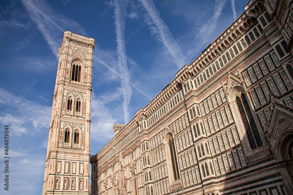 The side facade of the Florence Cathedral, Duomo of Santa Maria del Fiore with blue sky, famous bell tower with blue sky and scattered white clouds. UNESCO world heritage site in Italy, Tuscany.