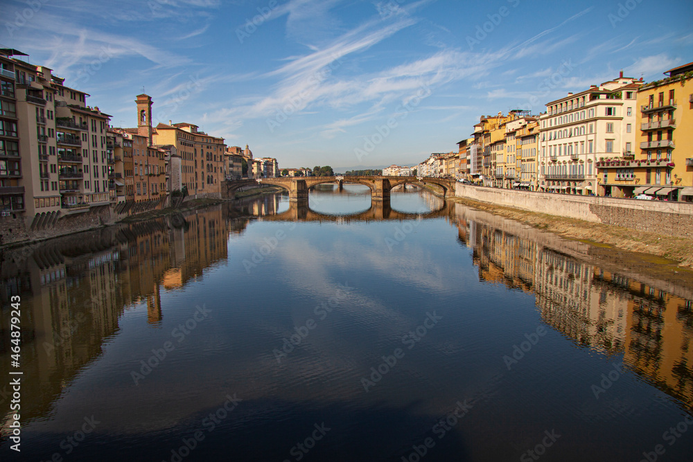 Beautiful view down the river Arno with Ponte Alle Grazie in Florence, Italy and italien houses of both sides reflecting in the water and blue sky background.