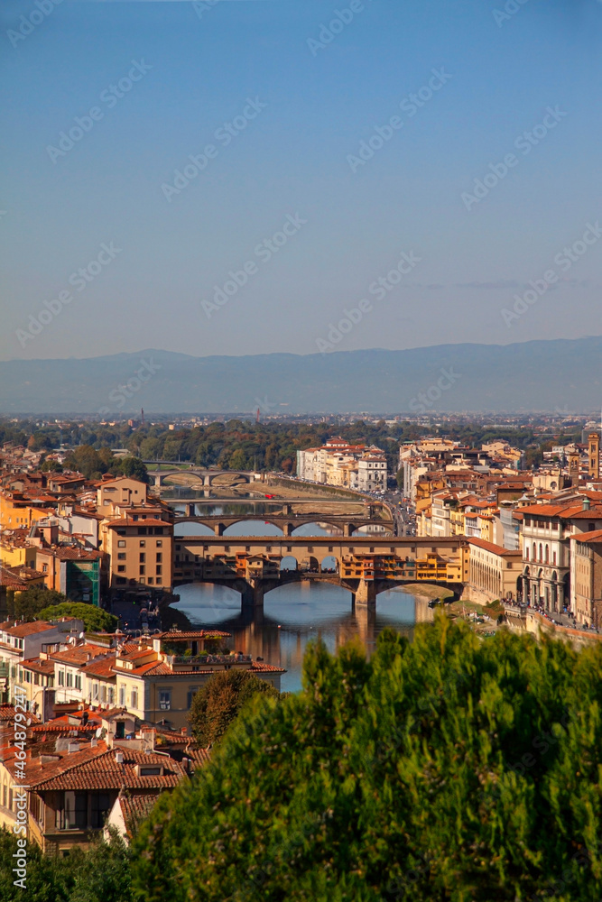 Aereal view of the famous Ponte Vecchio - in Florence (Firenze), Italy by the river Arno with reflections in the water and blue sky with a view over the city and the Italian house rooftops.