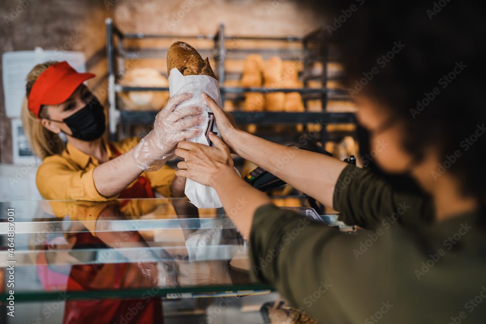 Obraz premium African American woman with protective face mask buying fresh bread in bakery.