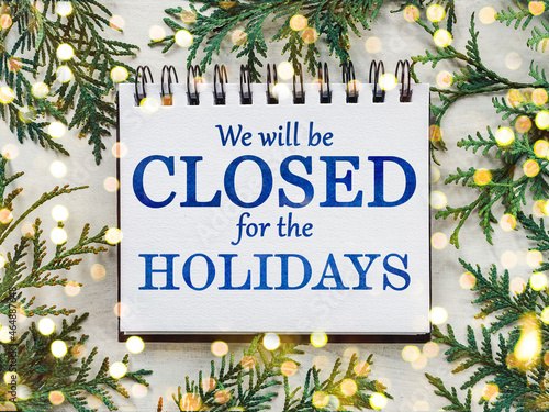 Signboard with the inscription We will be closed for the holidays and green branches of a Christmas tree. View from above, closeup, indoors, no people. Congratulations for family, friends, colleagues